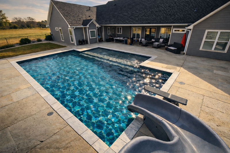 Luxury rectangular backyard swimming pool with clear blue water, diving board, and covered patio at a custom East Texas home.